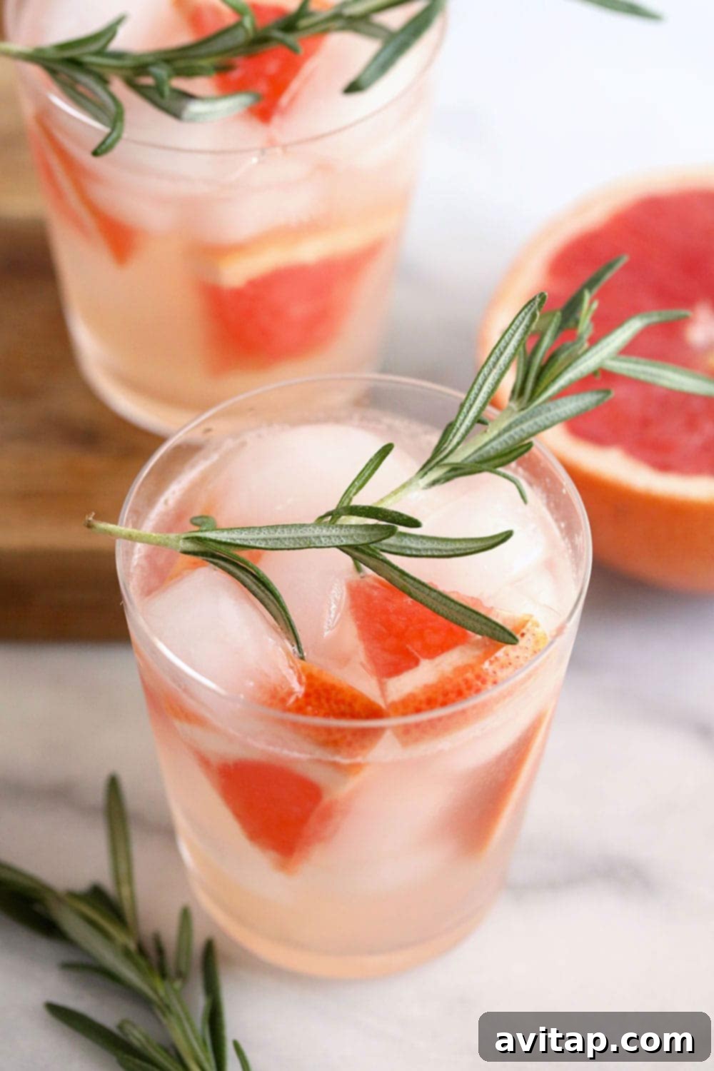 A tall glass containing a pink grapefruit hard seltzer, garnished with a grapefruit wedge and a sprig of fresh rosemary.