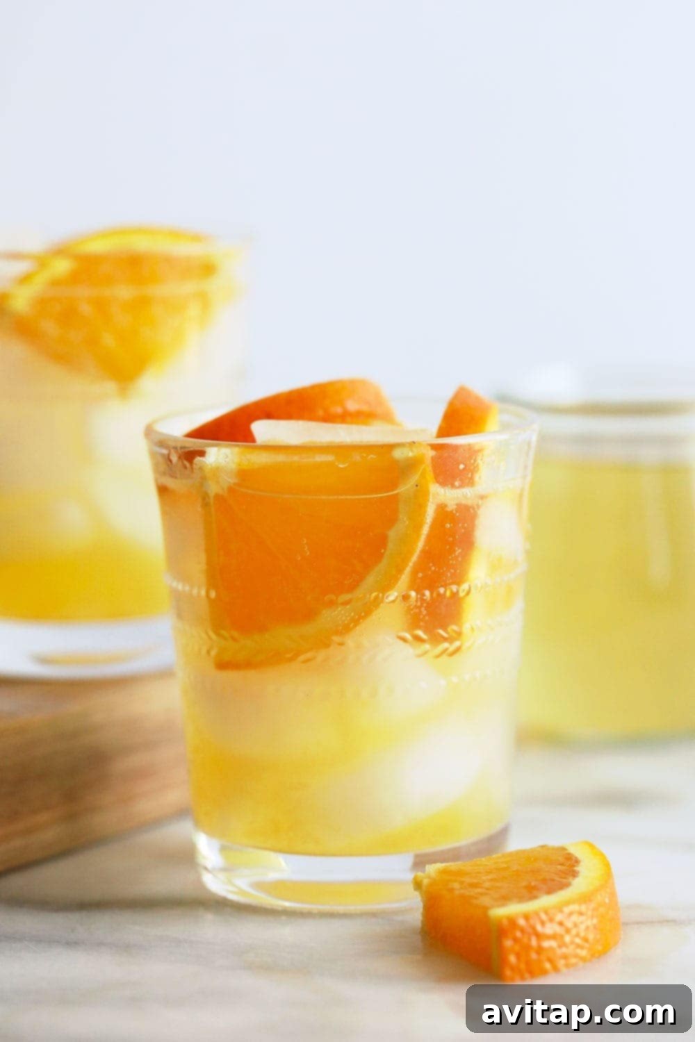 A glass filled with an amber-hued orange ginger hard seltzer, garnished with a vibrant orange wedge.
