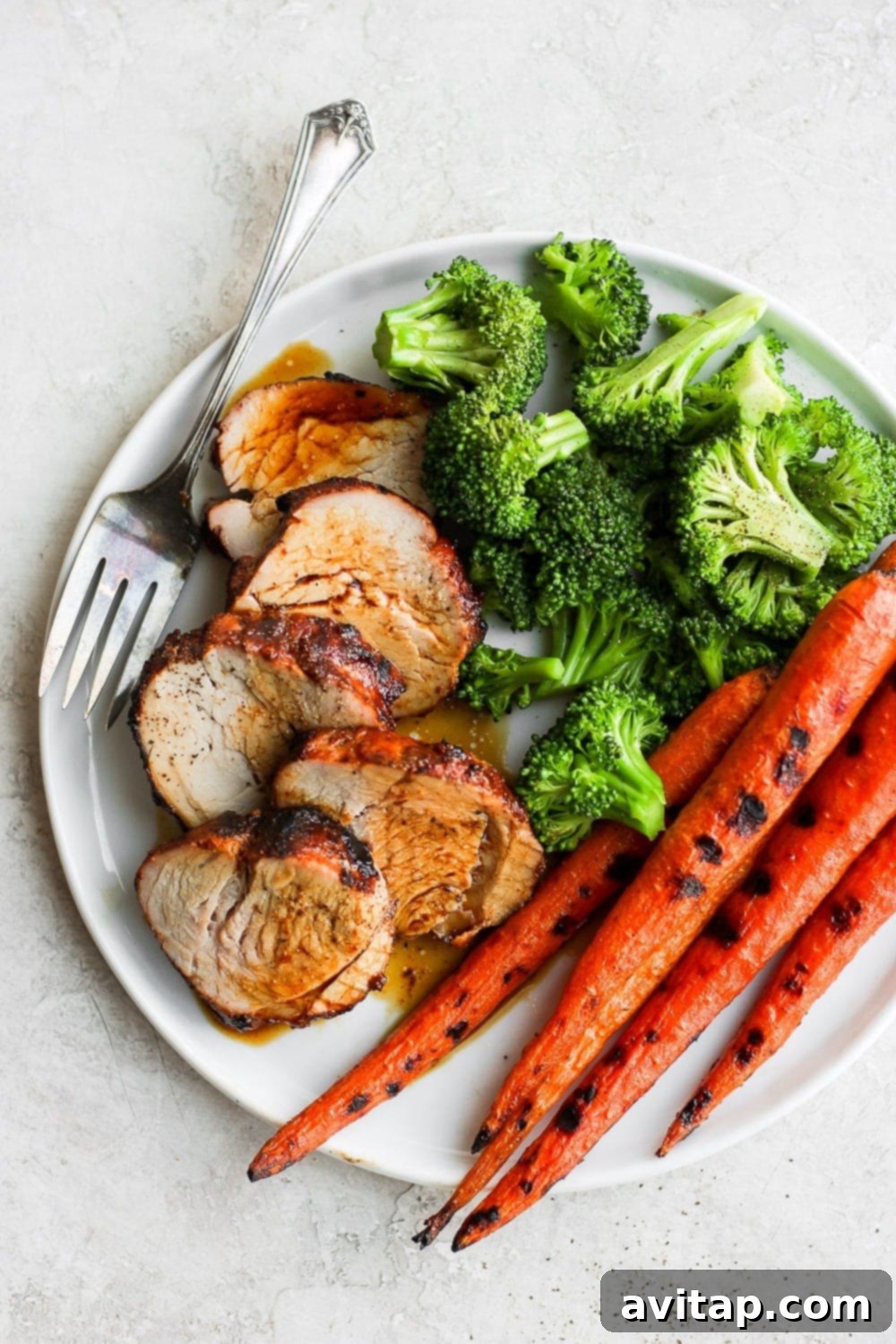 Sliced grilled pork tenderloin served with vibrant roasted vegetables on a white plate, highlighting its juicy interior.