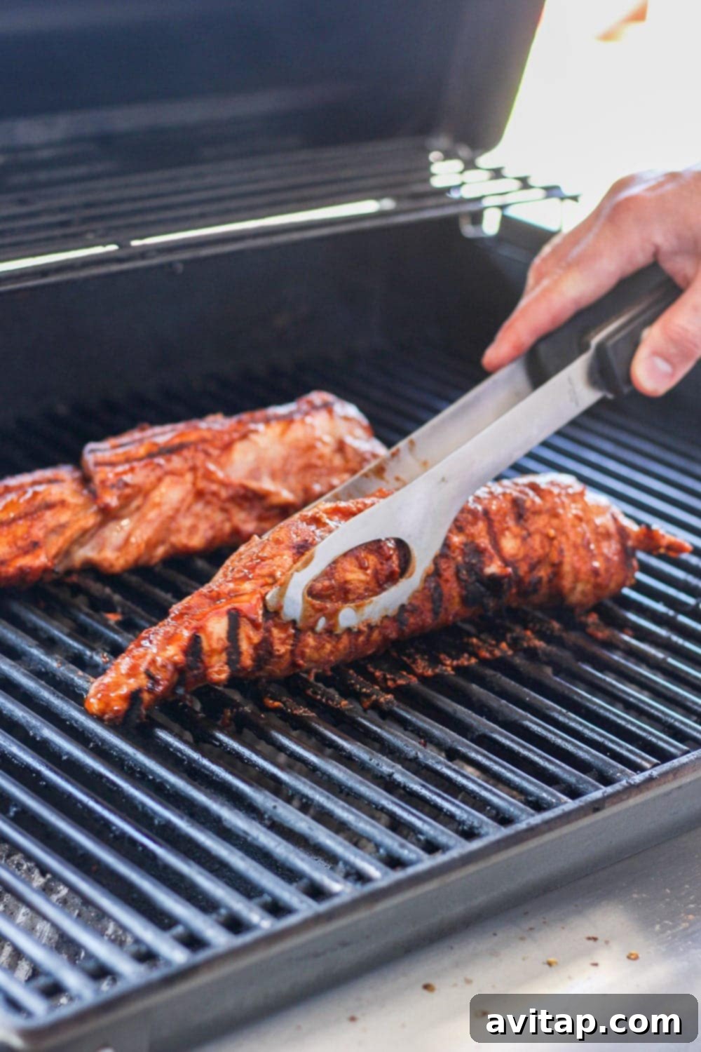 Two perfectly grilled pork tenderloins with distinct char marks resting on a grill grate.