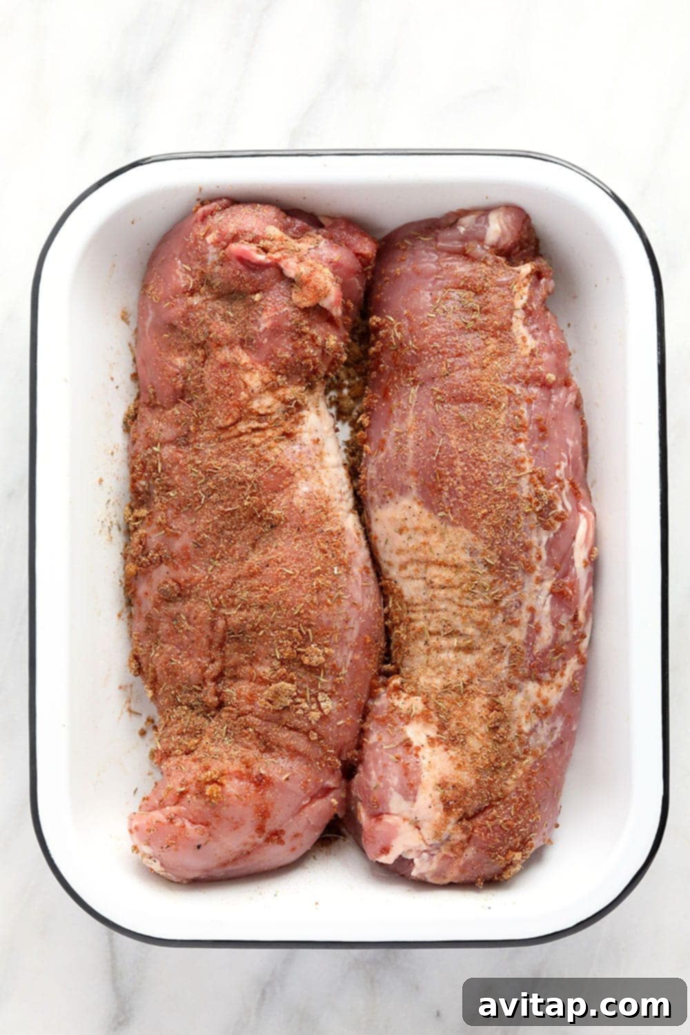 Dry rubbed pork tenderloin on a plate, ready for searing.