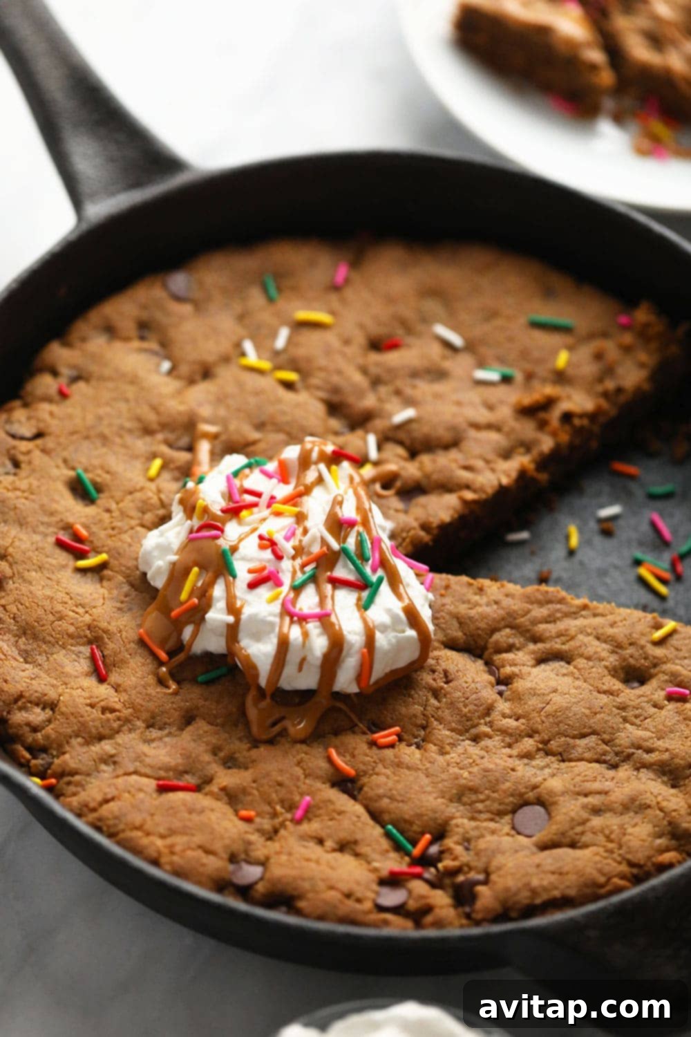 Delicious flourless peanut butter skillet cookie in a cast iron pan, topped with whipped cream and colorful sprinkles, ready for serving at a party or birthday celebration.