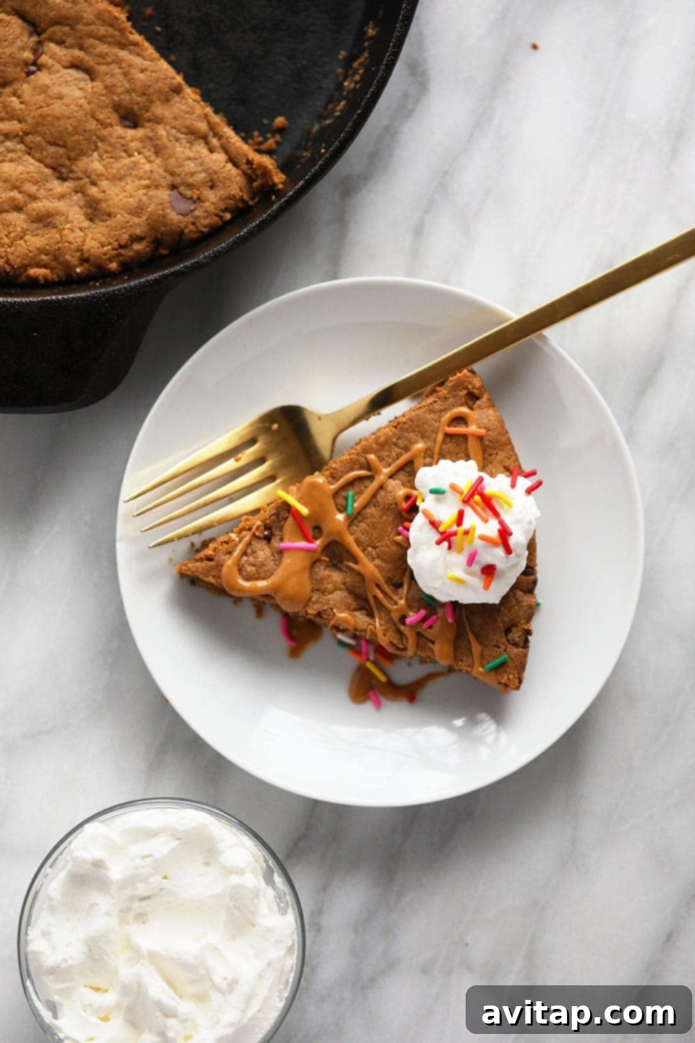 A delectable slice of healthy peanut butter skillet cookie on a plate, adorned with light whipped cream and vibrant sprinkles, ready to be enjoyed.