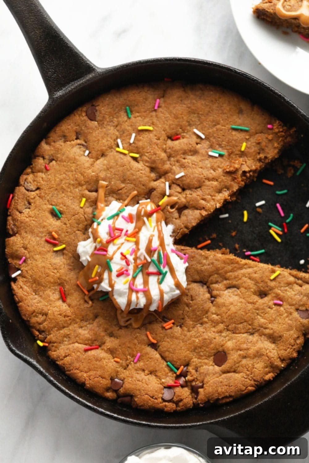 Close-up of a delightful peanut butter skillet cookie, generously topped with fluffy whipped cream and vibrant sprinkles, ready to be enjoyed.
