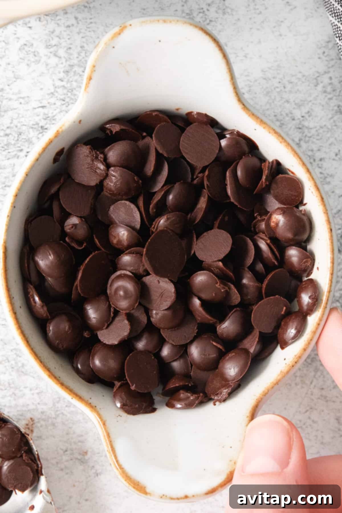 A person's hand reaching into a bowl of homemade vegan chocolate chips, ready to grab a handful, suggesting the irresistible nature of the treat.