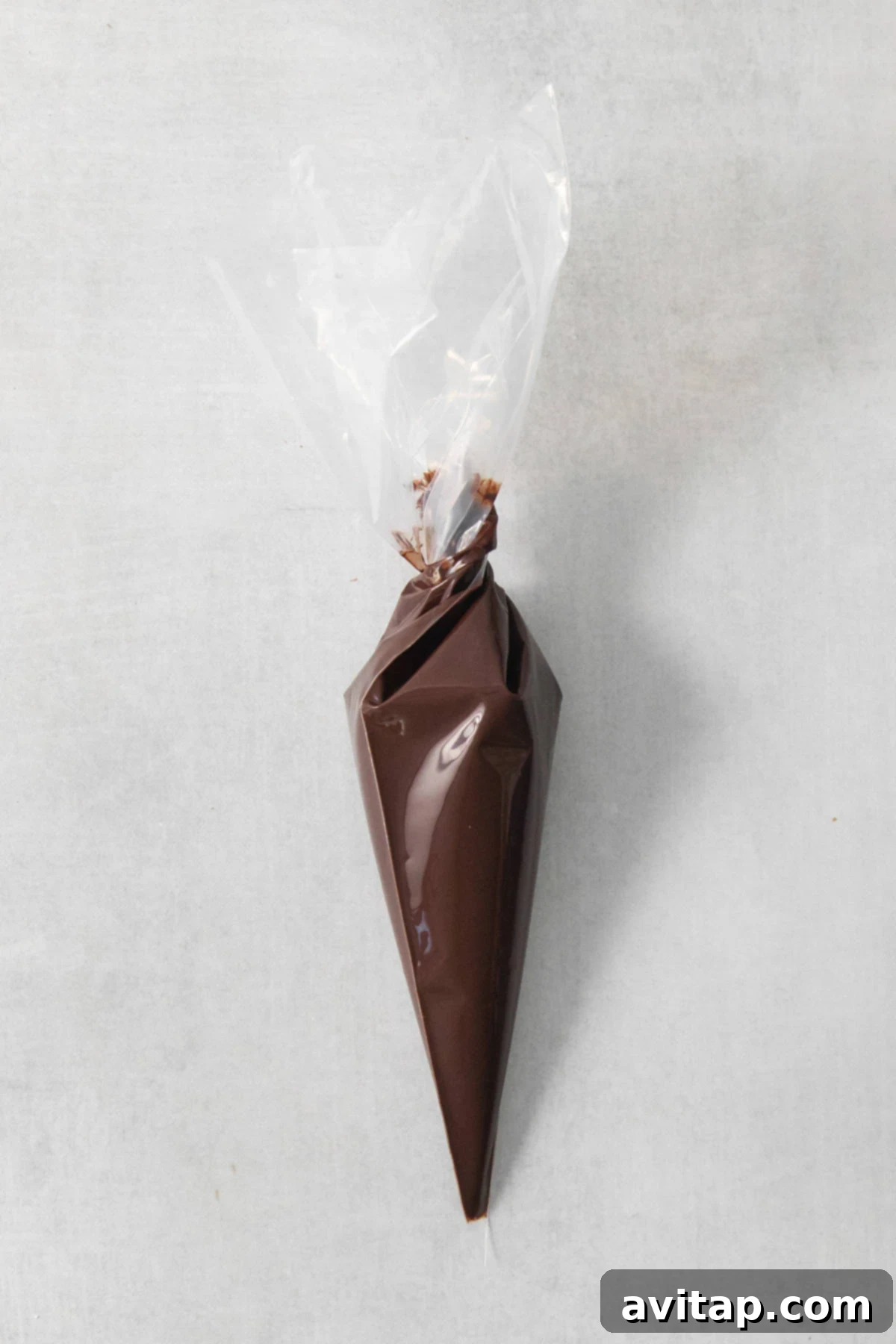 Melted chocolate mixture neatly contained within a piping bag, ready to be transformed into vegan chocolate chips on a rustic concrete surface.