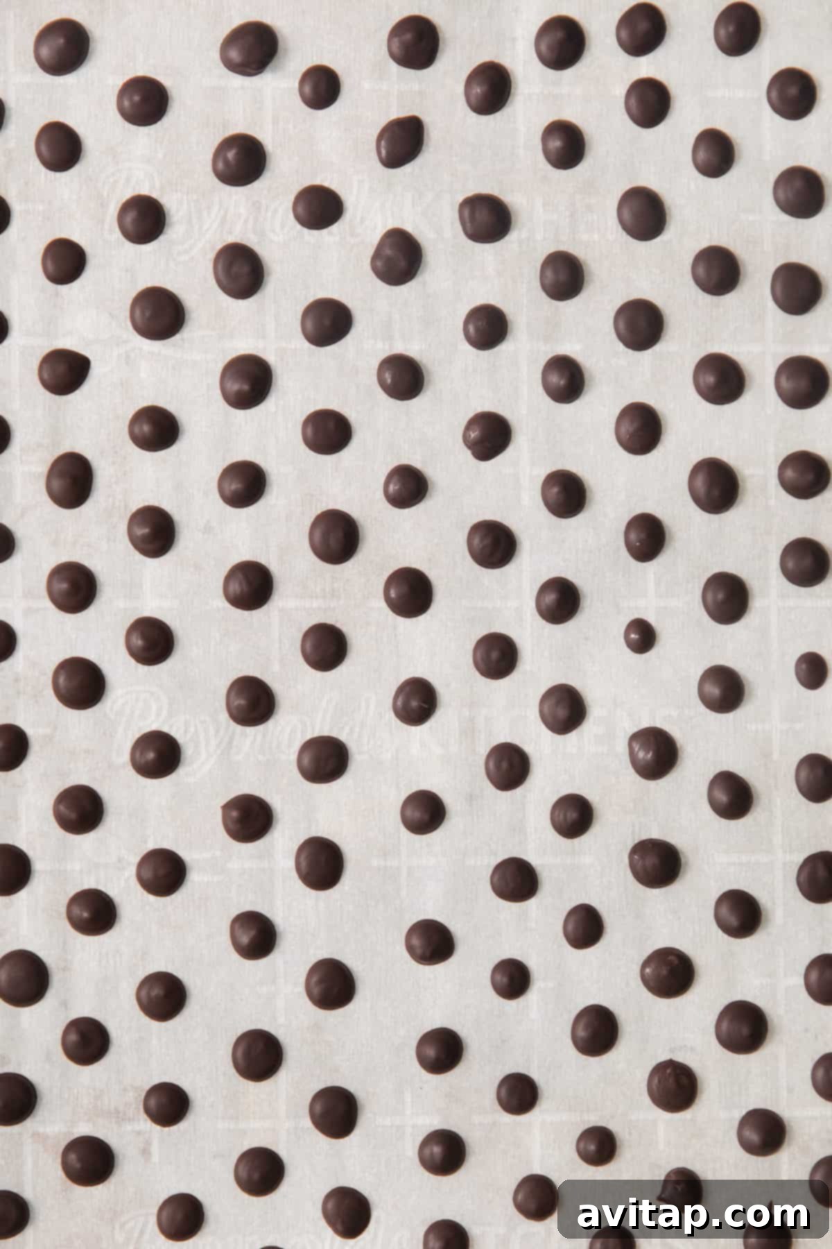 A pristine white surface dotted with perfectly piped and hardened homemade vegan chocolate chips, showcasing their uniform size and readiness for use.