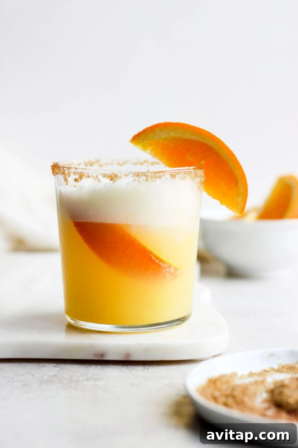 Velvet Orange Dream 2 A vibrant orange cocktail in a tall glass, topped with a luscious froth. The glass is elegantly garnished, ready to be enjoyed.