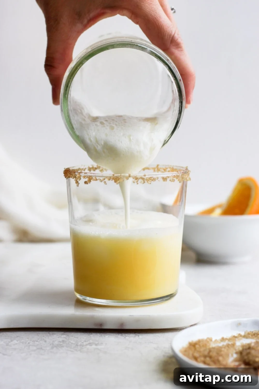 Velvet Orange Dream 5 The frothy, creamy mixture of the orange creamsicle cocktail being carefully poured from a shaker into a sugar-rimmed glass.