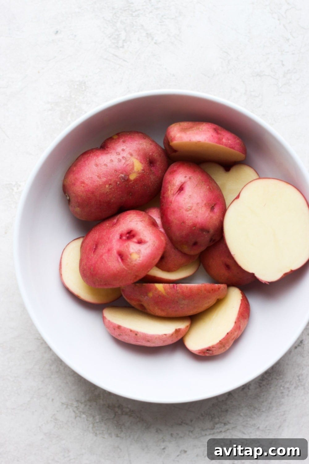 Selecting small red potatoes of similar size for optimal smashed potato results. Raw red potatoes in a bowl, perfectly sized and ready for boiling to make smashed potatoes.