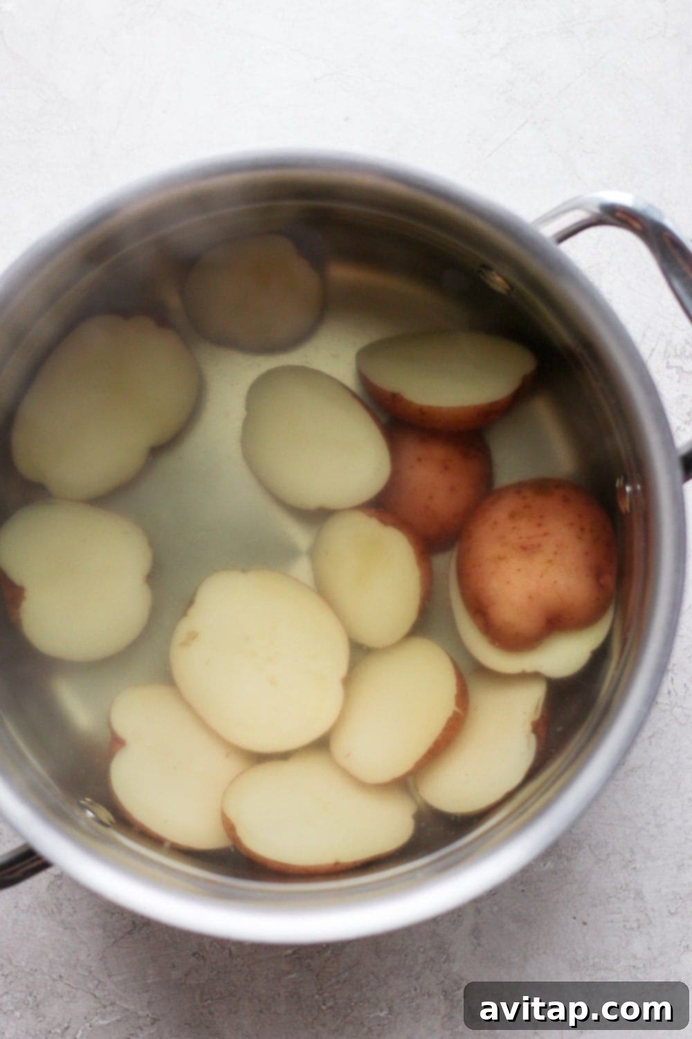 The initial boil: ensuring red potatoes are tender before smashing. Red potato halves boiling in a large pot of salted water on the stovetop.