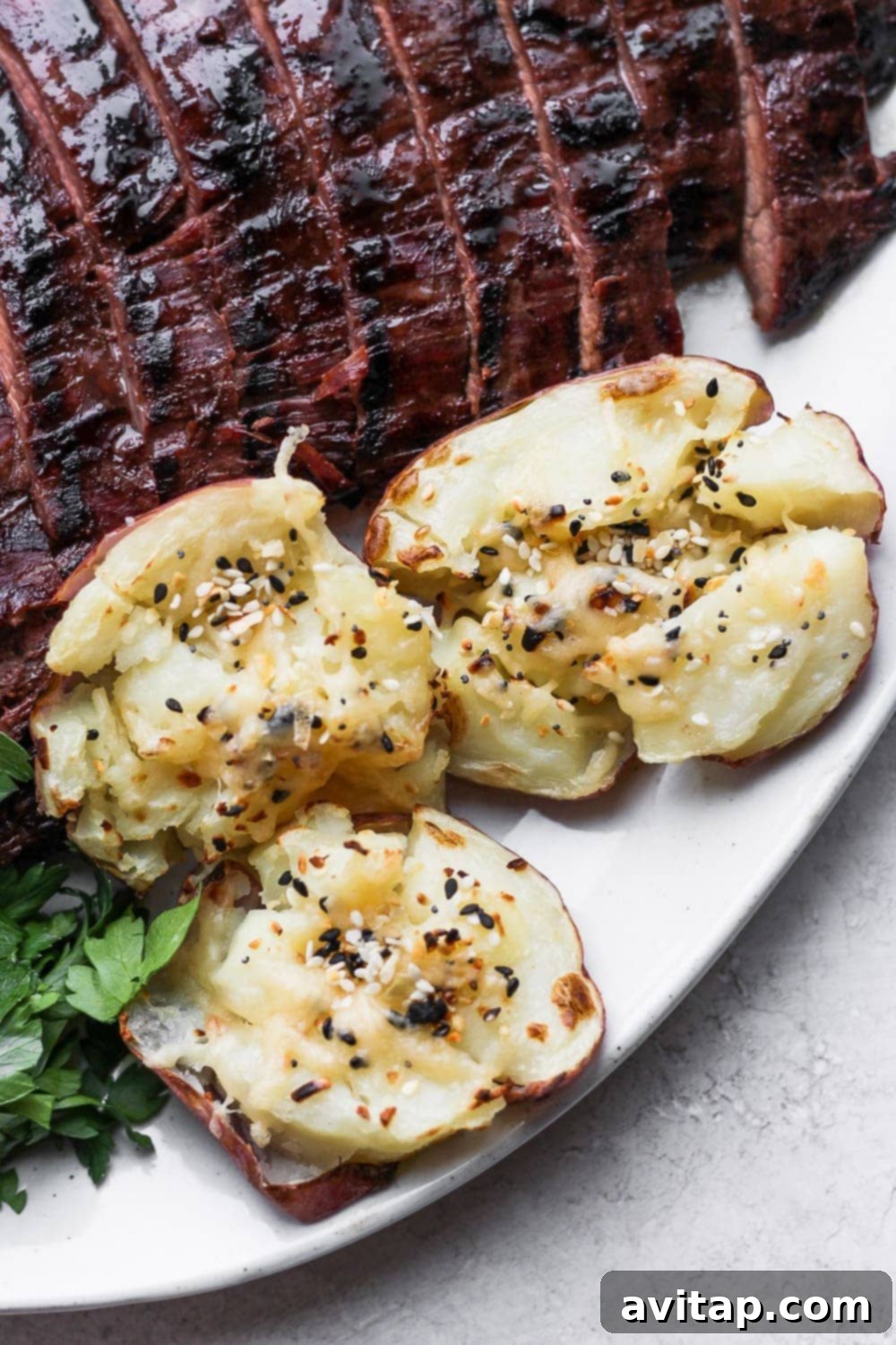 The perfect pairing: crispy smashed red potatoes and succulent flank steak. Smashed red potatoes served alongside a perfectly cooked flank steak on a rustic plate.
