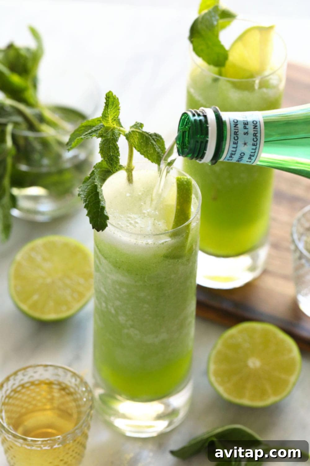Close-up shot of sparkling water being poured into a tall glass filled with a vibrant green frozen mojito, creating effervescent bubbles.