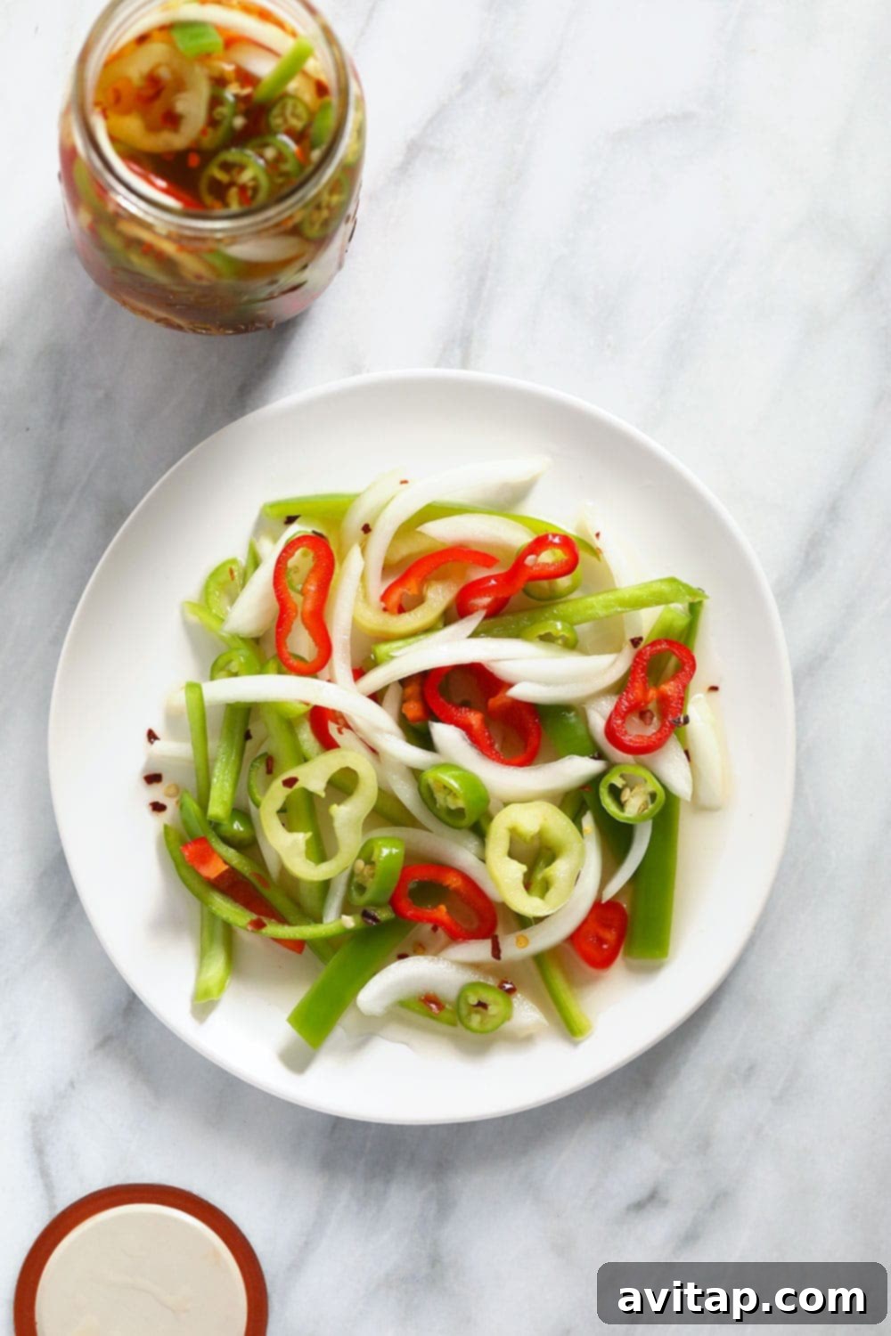 Individual ingredients for quick pickled peppers, including various sliced peppers, garlic, and vinegar bottles, neatly arranged on a plate.