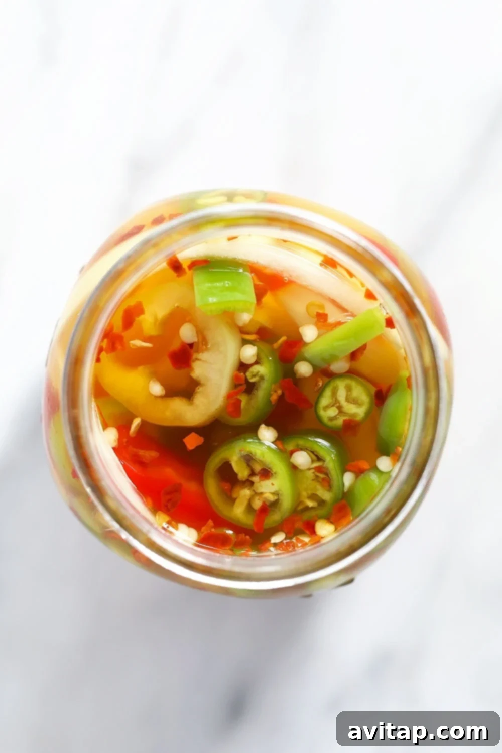 A mason jar filled with sliced peppers, garlic, and onions, submerged in clear pickling brine, undergoing the pickling process in the refrigerator.