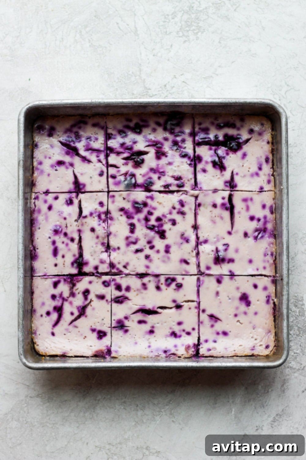 These blueberry cheesecake bars are perfectly baked, awaiting their final chill before being enjoyed. Baked lemon blueberry cheesecake bars in a square baking dish, cooled and ready for slicing.