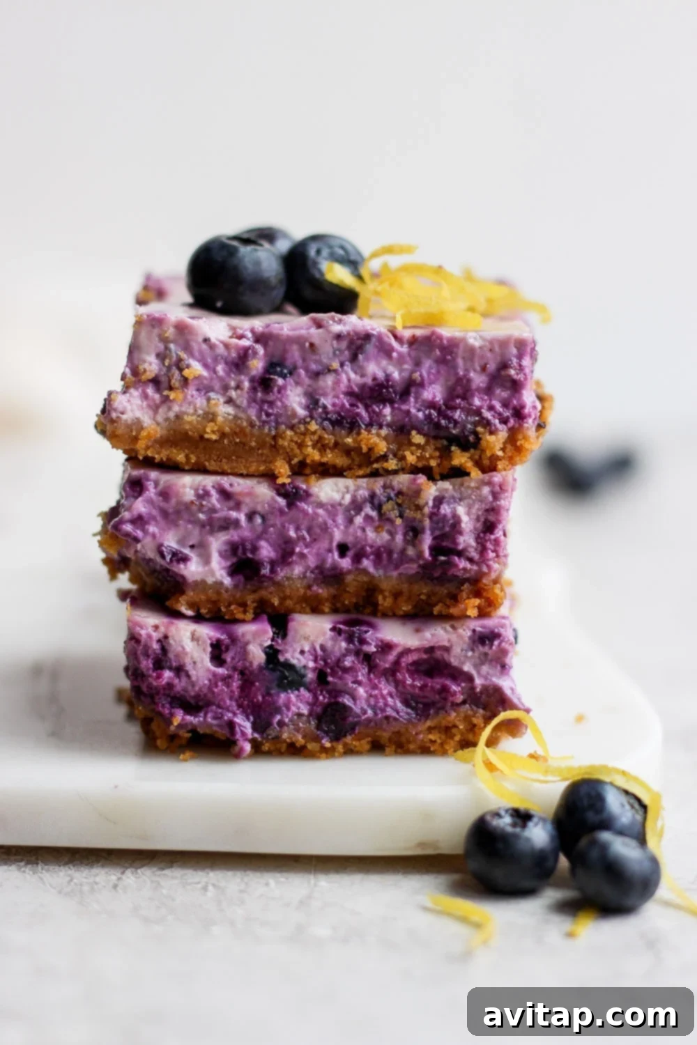 These delightful blueberry cheesecake bars are a beautiful and delicious treat for any occasion. Three perfectly stacked blueberry cheesecake bars, topped with fresh berries and lemon zest, ready to be enjoyed.