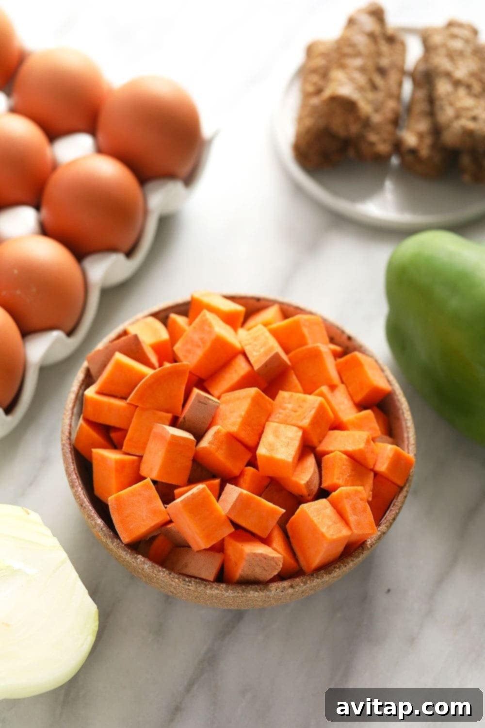 Raw ingredients for sweet potato hash laid out: sweet potatoes, eggs, breakfast sausage, a bell pepper, and an onion.