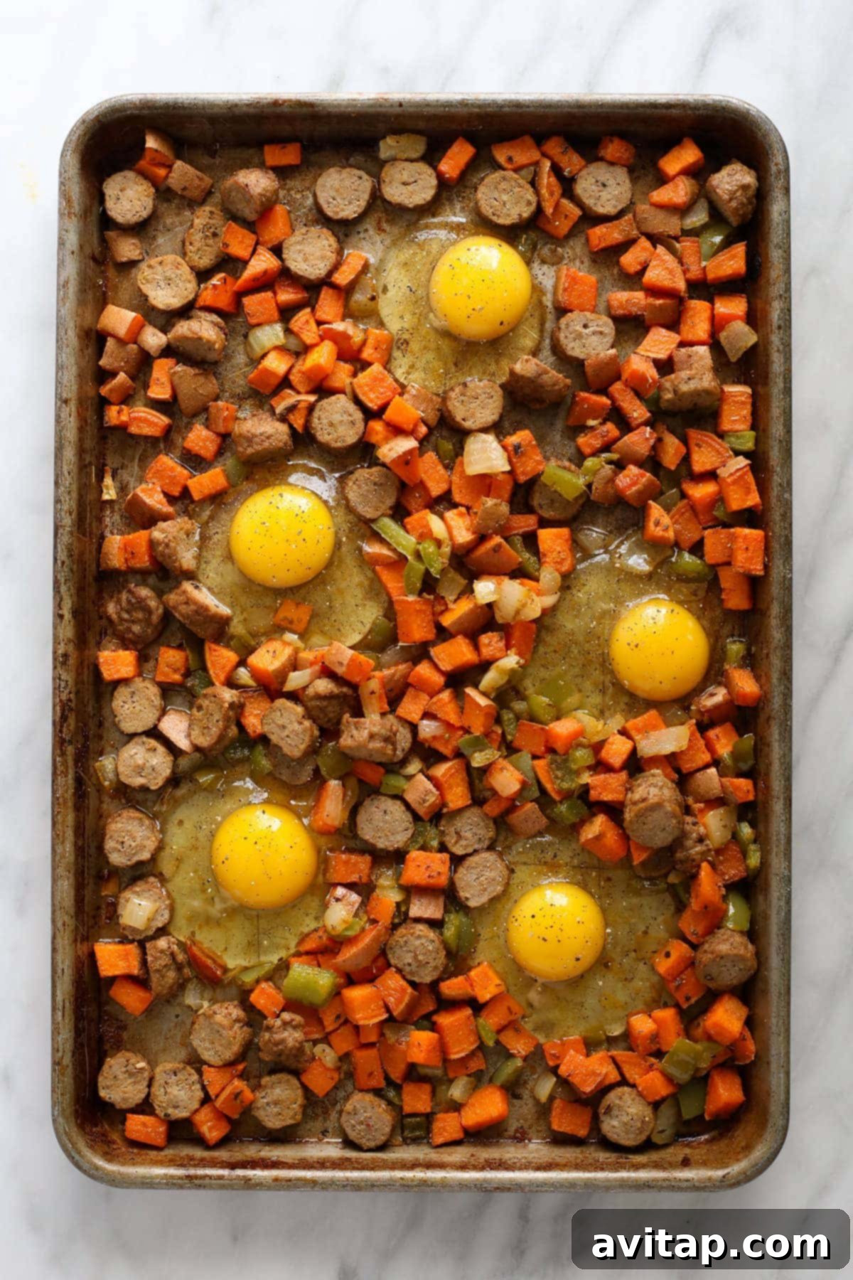 Sweet potato hash on a sheet pan with nests created and raw eggs cracked into them, ready for final baking.