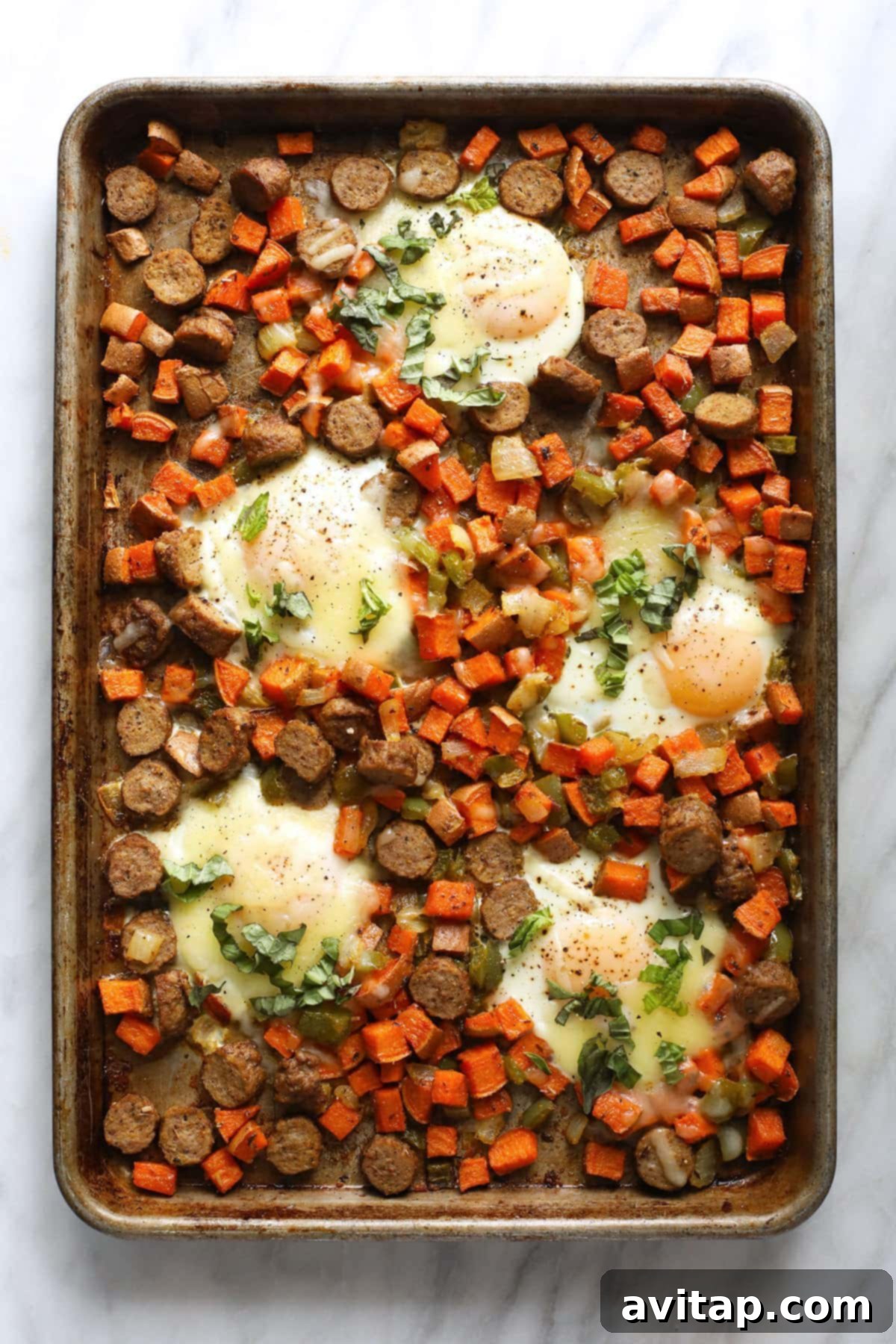 Sheet pan filled with finished sweet potato hash and baked eggs, topped with melted cheese.