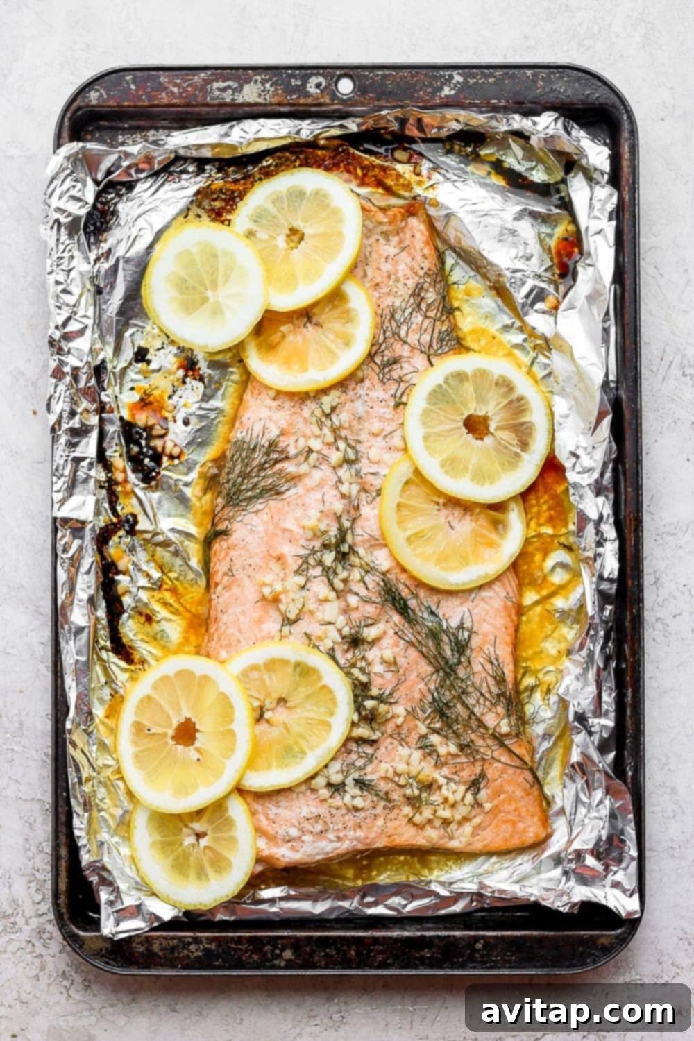 Large salmon fillet on tin foil with fresh lemon slices and dill, ready for oven baking. A delicious and healthy meal option.