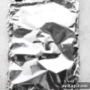 Sheet pan with salmon completely wrapped and sealed in aluminum foil.