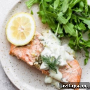 Cooked salmon on a plate, garnished with fresh dill and served with a side of tartar sauce.
