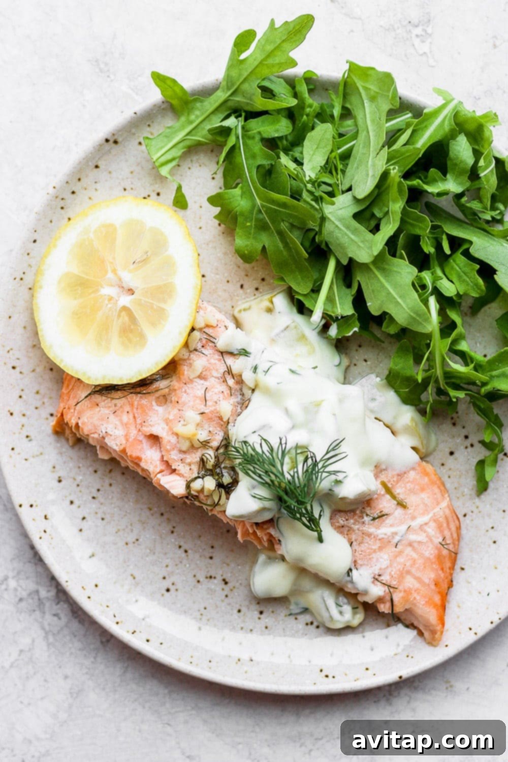 Perfectly cooked salmon portion served on a plate with fresh arugula, a lemon wedge, and a generous dollop of homemade tartar sauce, highlighting a complete meal.