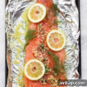 Salmon on foil with fresh dill and lemon slices placed directly on top.