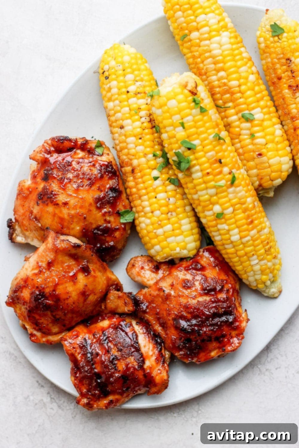 Delicious Grilled Chicken Thighs Meal Two grilled chicken thighs with corn on the cob on a white plate, ready to be served.