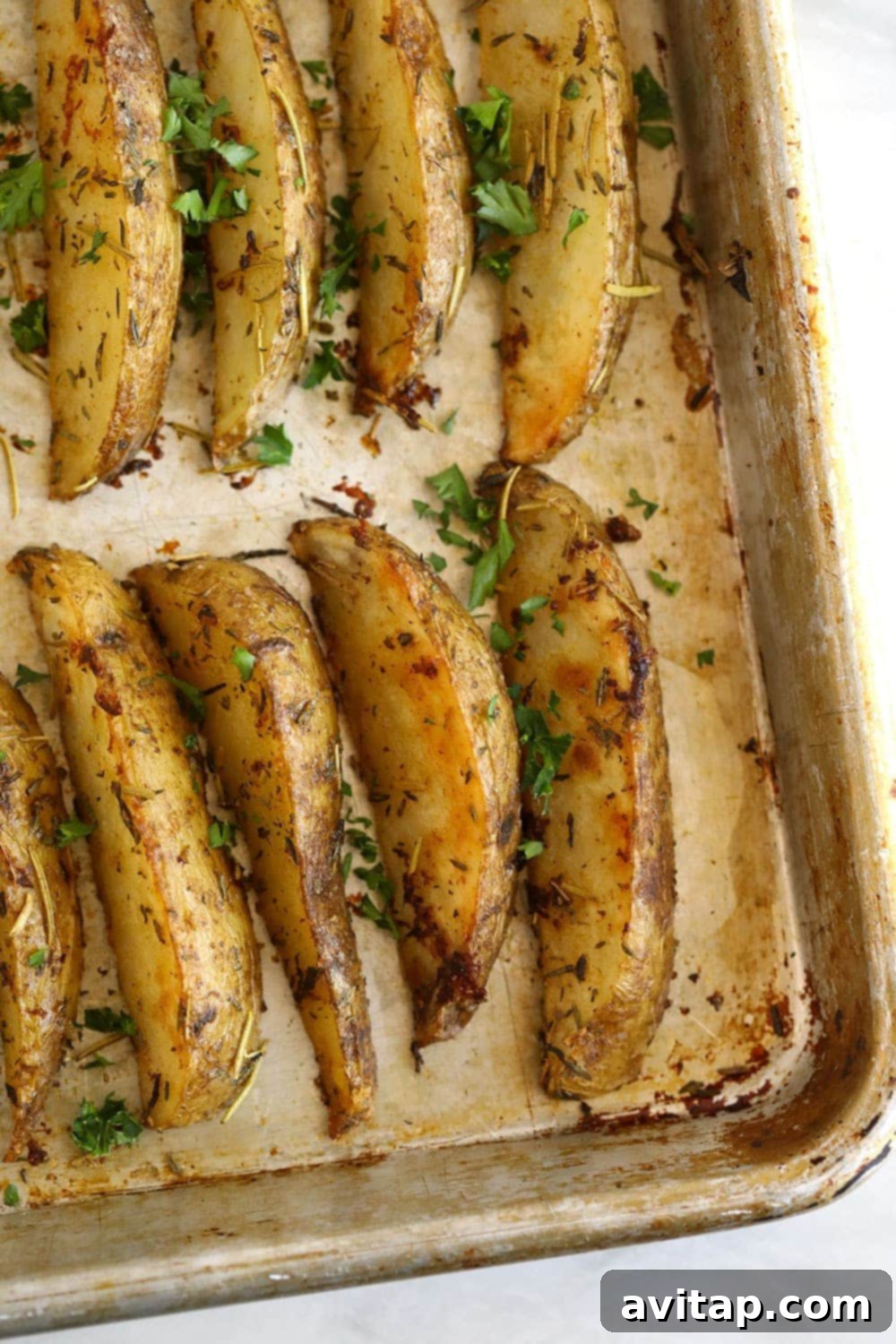 Baked potato wedges on a baking sheet, garnished with fresh parsley.