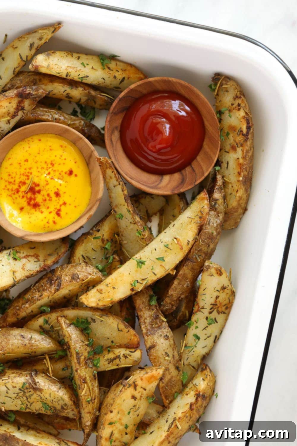 Oven-baked potato wedges in a pan, served with small bowls of ketchup and mustard.