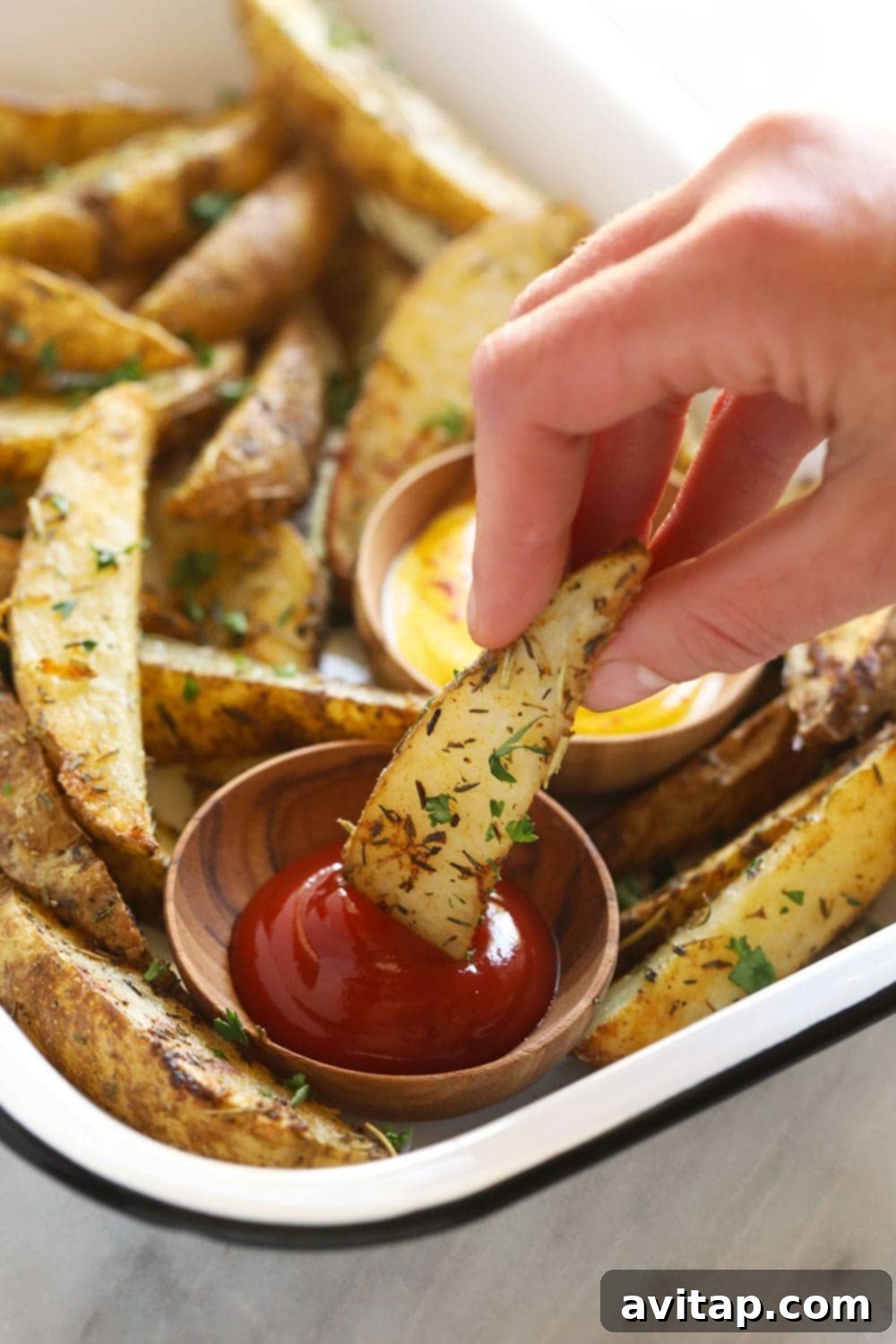 Close-up of a potato wedge being dipped into ketchup.