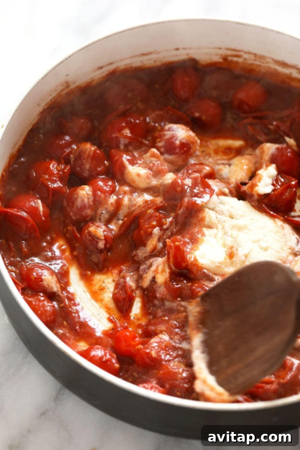 A spoonful of creamy ricotta cheese being added to the simmering tomato sauce in a skillet, creating a rich texture.