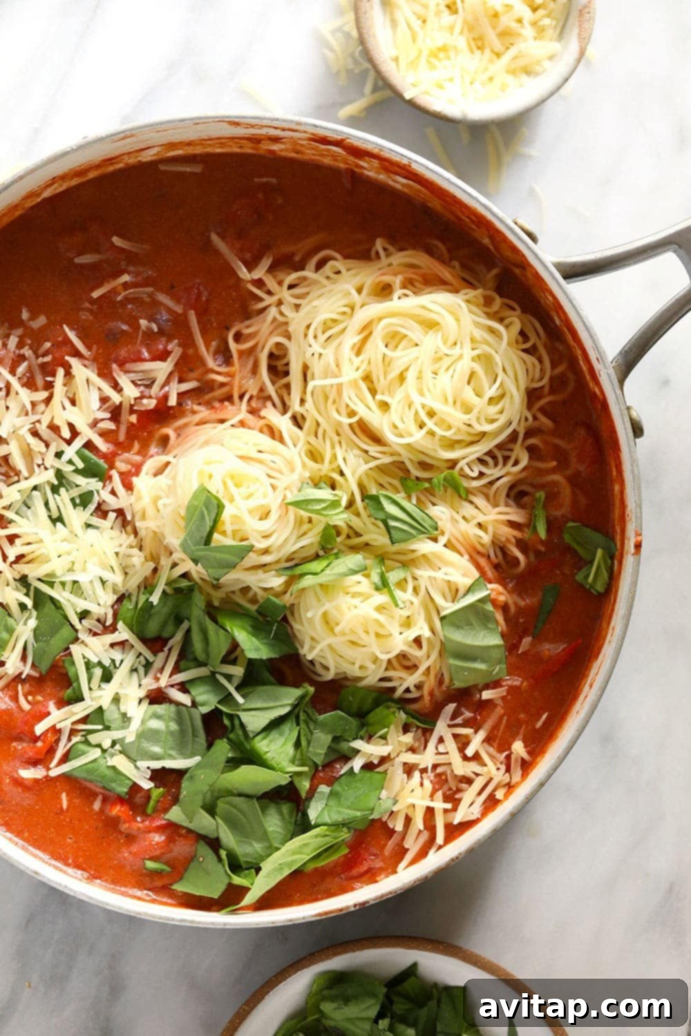 A beautifully plated bowl of garden summer pasta, generously topped with fresh parmesan cheese and fragrant basil leaves.
