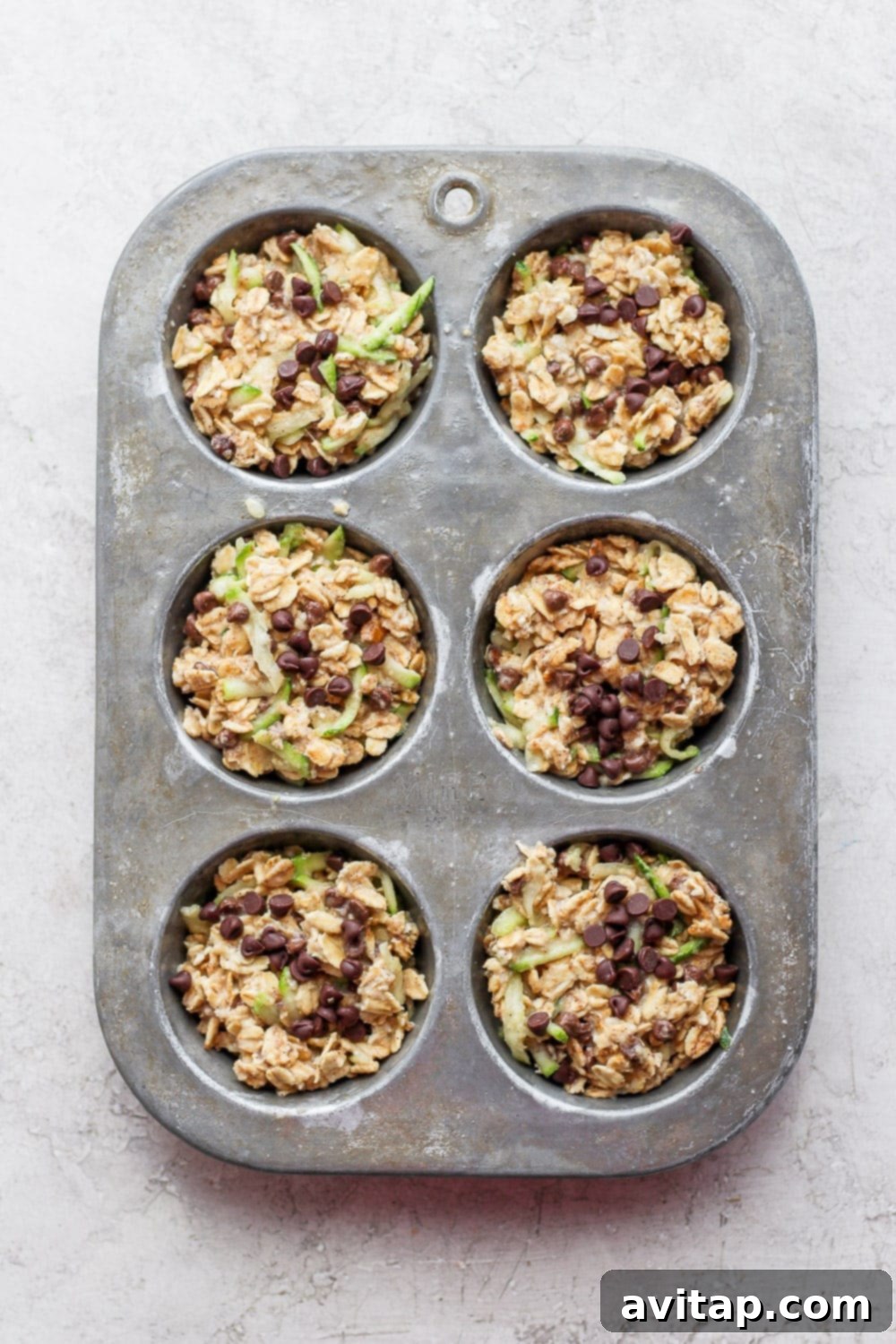 Unbaked zucchini oatmeal cup batter portioned into a muffin tin, ready for the oven.