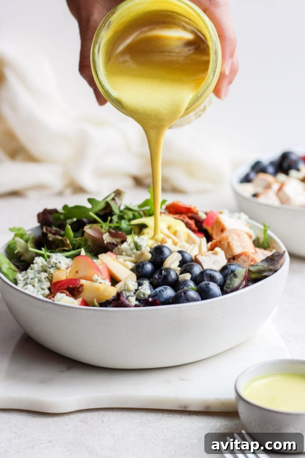 Chargrilled Chicken Garden Salad 7 Pouring honey mustard dressing onto chicken salad in a bowl. This grilled chicken salad recipe is made with easy grilled chicken, greens, blueberries, apple, gorgonzola, bacon, slivered almonds, and a homemade creamy honey mustard dressing.