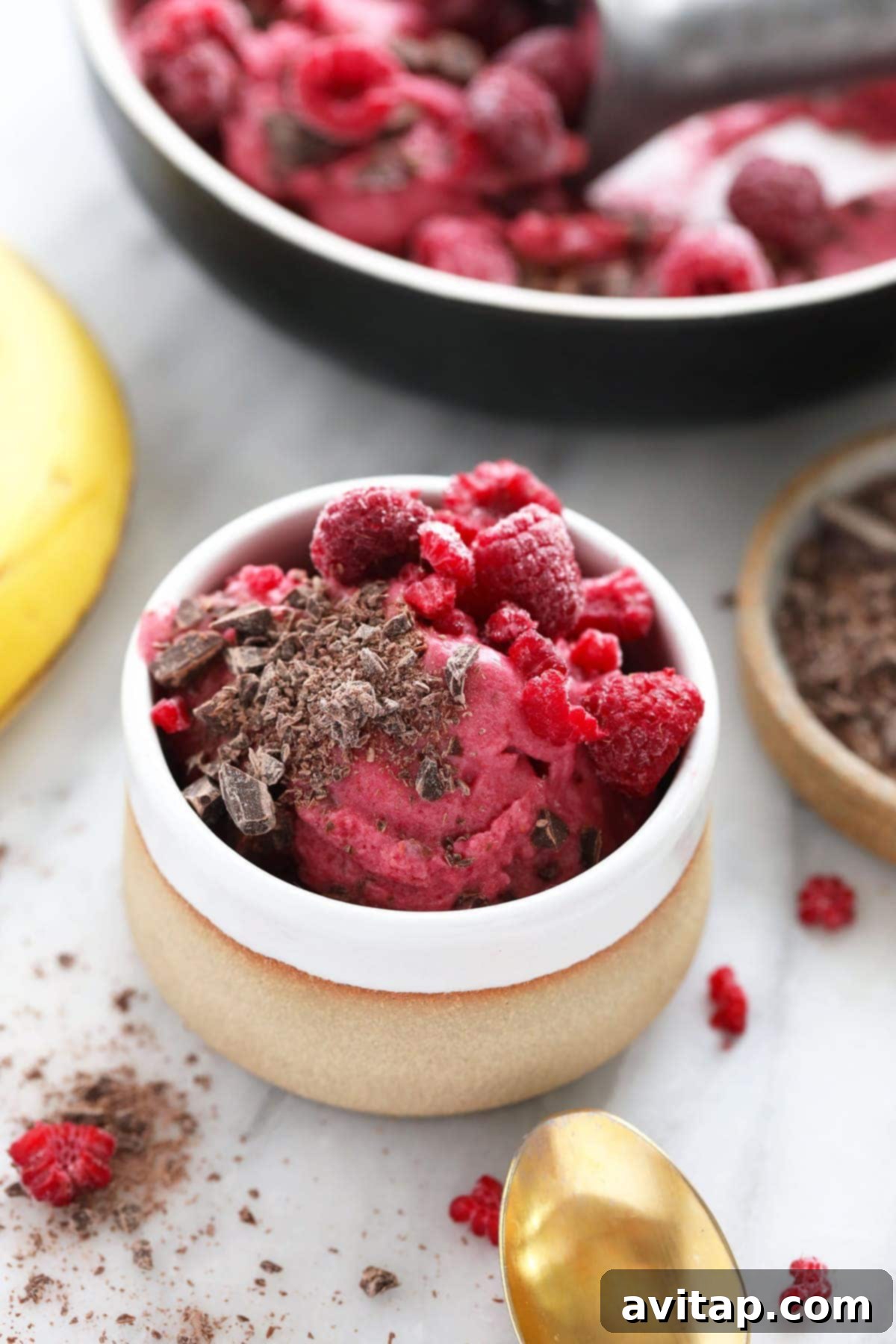 A vibrant bowl of Raspberry Chocolate Chunk Nice Cream, beautifully topped with fresh, glistening raspberries, ready to be enjoyed.
