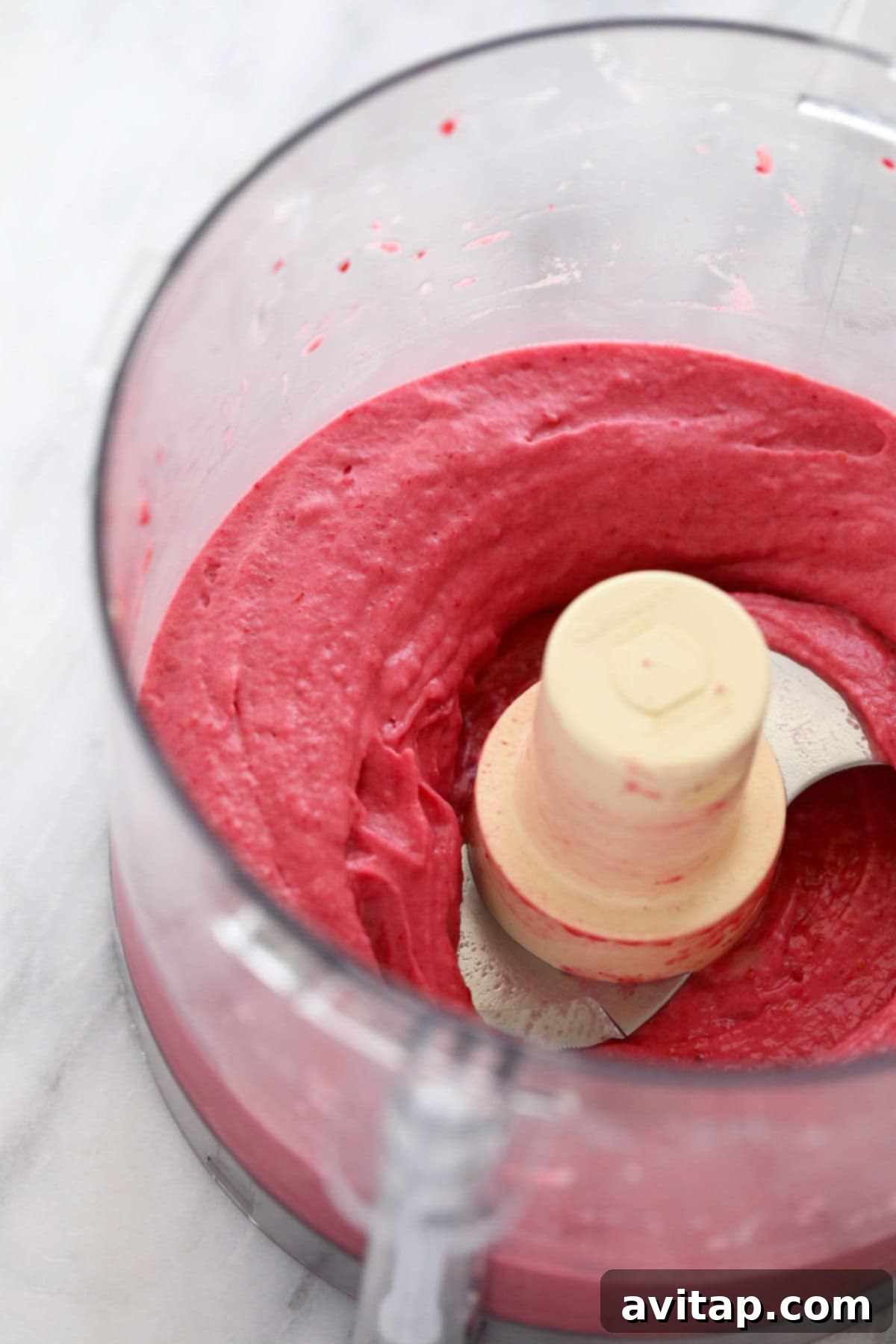 Perfectly blended raspberry banana nice cream, smooth and creamy, swirling in a food processor, signaling it's ready for chocolate chunks and serving.