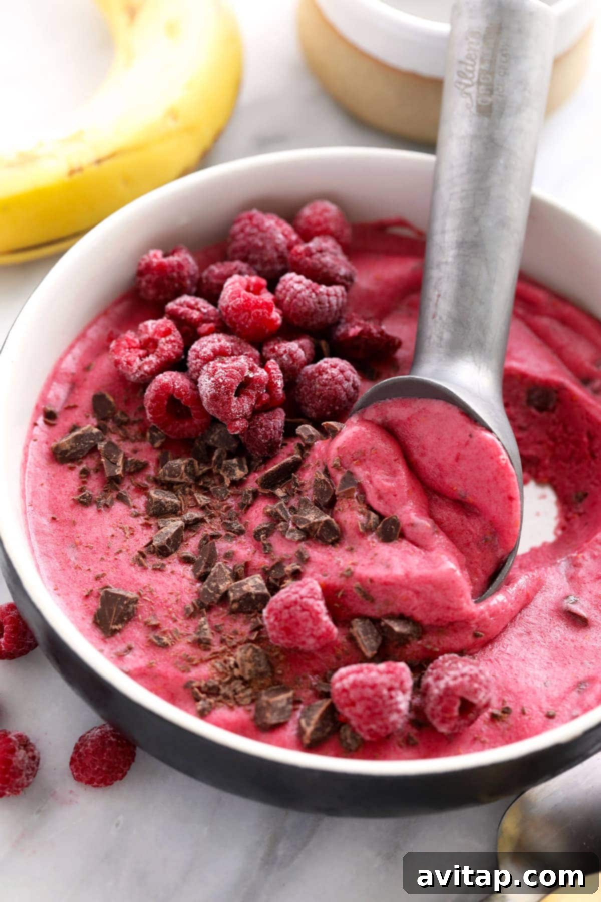 A scoop of rich, creamy Raspberry Chocolate Chunk Nice Cream being lifted from a bowl with an ice cream scooper, highlighting its perfect soft-serve consistency.