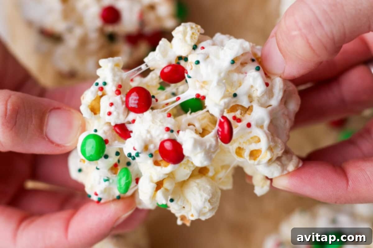 Hands holding a Christmas popcorn ball decorated with red and green candy-coated chocolates and festive sprinkles.