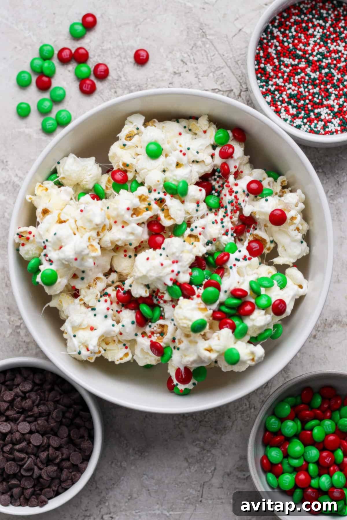 A bowl of Christmas popcorn surrounded by bowls of toppings.