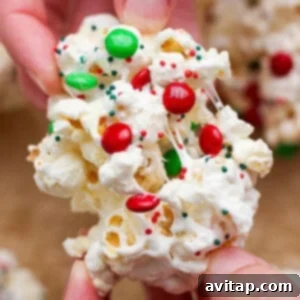 Close-up of hands holding a cluster of popcorn mixed with melted marshmallow, red and green candy-coated chocolates, and festive sprinkles.