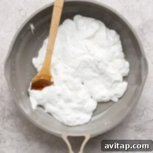 A nonstick skillet with a wooden spatula stirring a mound of whipped egg whites on a light textured surface.