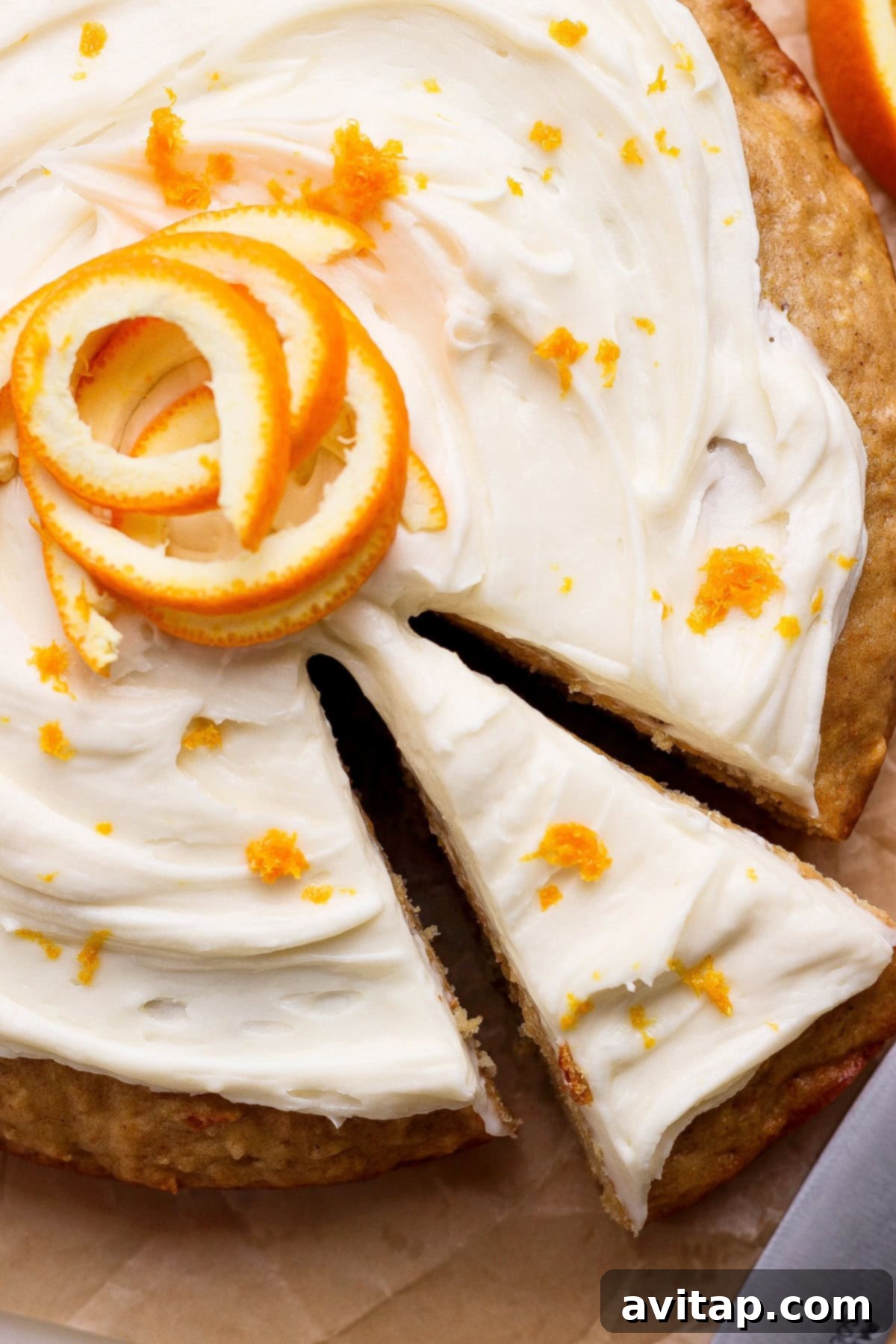 A fully frosted whole orange cake with a slice being removed.