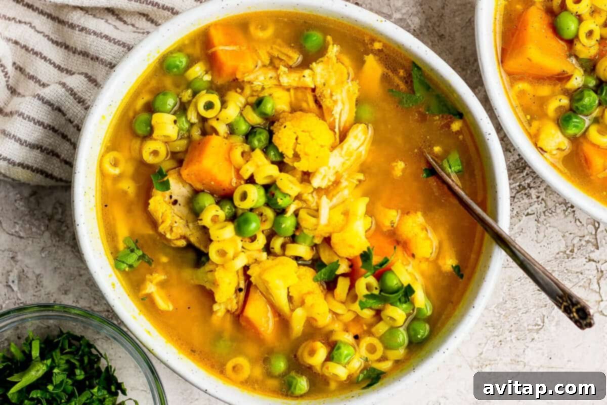 A bowl of vibrant yellow immunity soup with pasta, vegetables, and herbs.