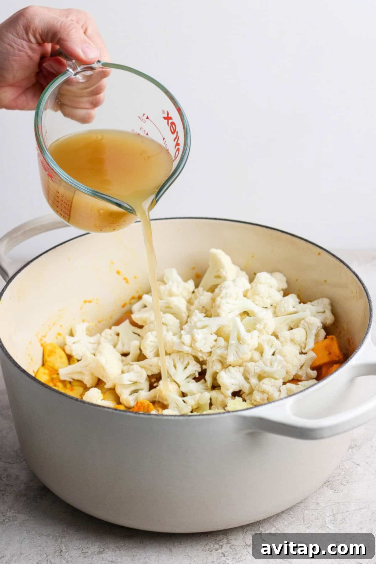 Pouring broth into a pot of vegetables.