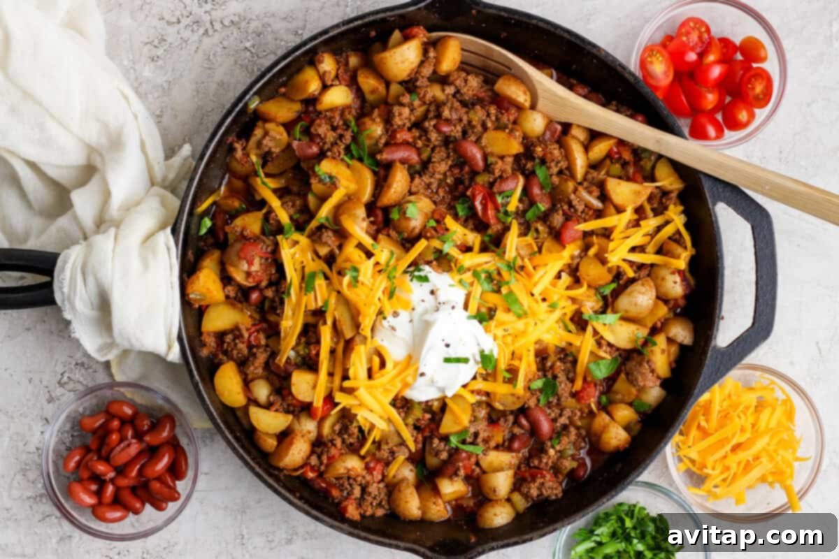 A delicious potato chili skillet topped with cheese, sour cream, and herbs.