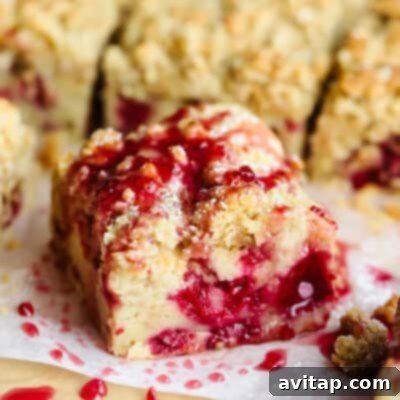 A close-up of a slice of crumb cake with a raspberry filling and a drizzle of raspberry sauce on top.
