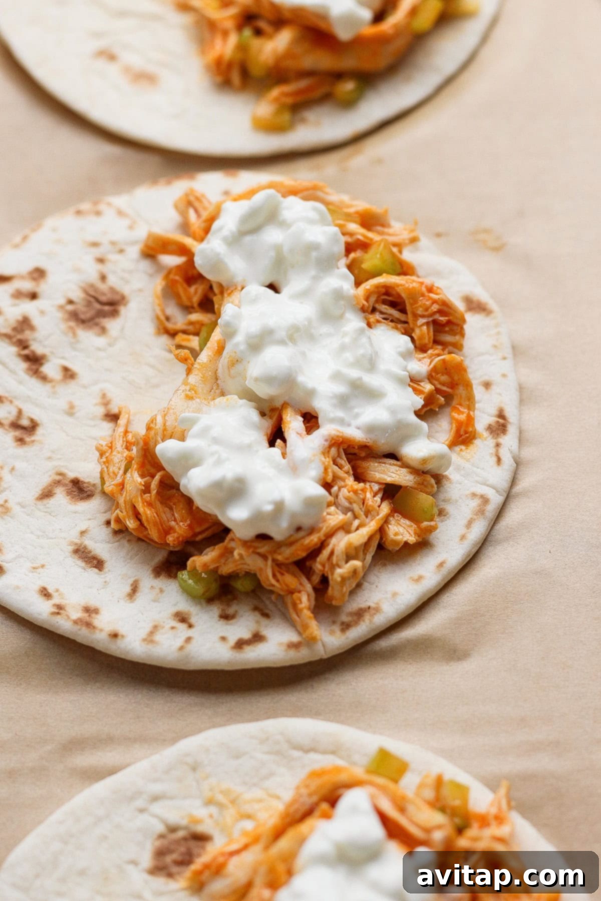 Assembling Buffalo Chicken Tacos - Flour tortillas filled with shredded chicken and vegetables.